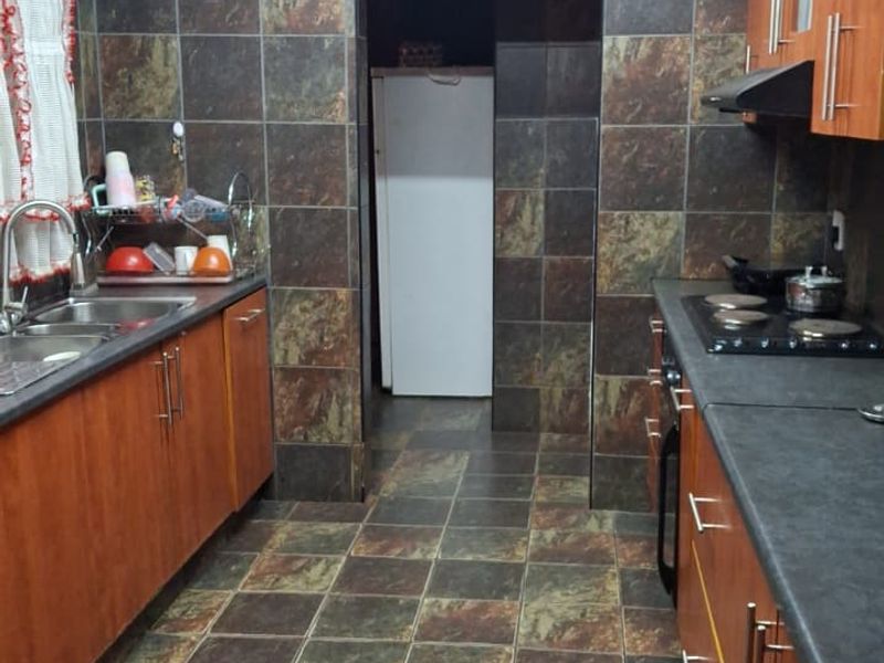 A functional kitchen featuring wood-finish cabinetry, dark laminate countertops, integrated hob with extractor, and full-height tiled wall finishes.