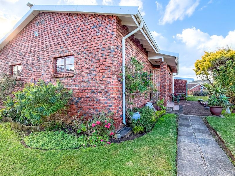 A well-maintained face brick apartment exterior featuring a paved walkway, patio area, and established garden surroundings.