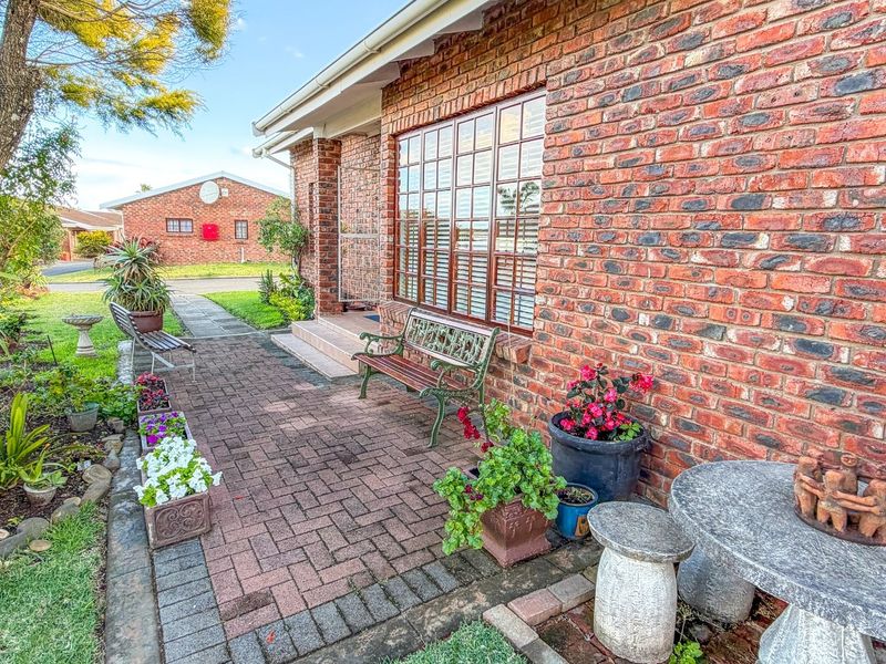 A paved rear patio area featuring a classic red brick exterior wall and timber-framed windows, set within a landscaped garden environment.