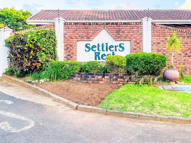 The entrance to Settlers Rest complex featuring a brick boundary wall, electric fencing, and established garden landscaping.