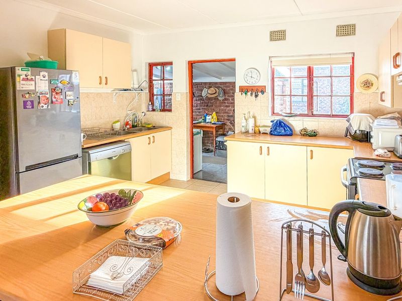 A functional kitchen featuring light-toned cabinetry, laminate countertops, tiled backsplash, and a central island, with direct access to an adjacent utility area.