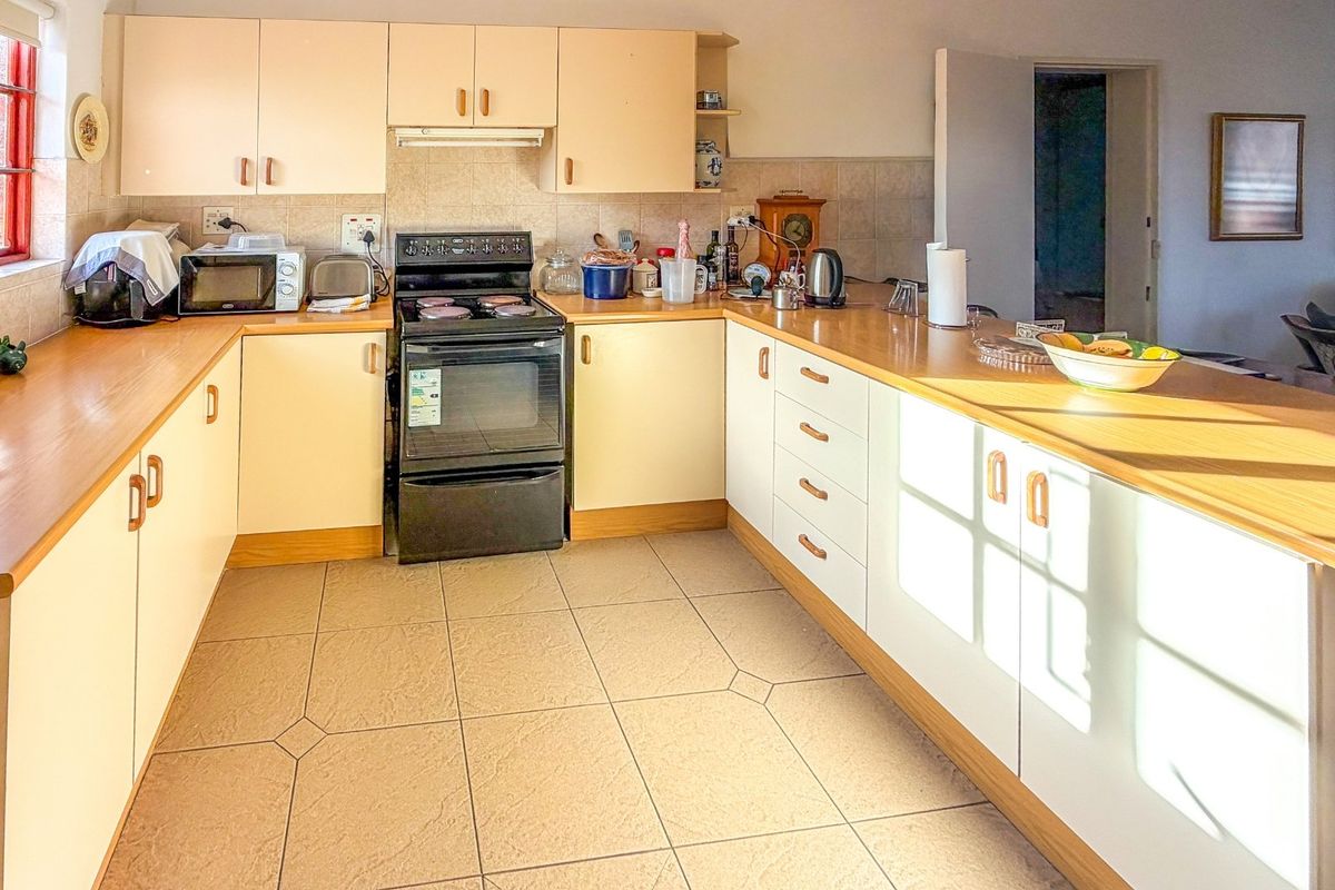 A functional kitchen featuring laminate countertops, tiled flooring, a tiled backsplash, and built-in cabinetry with a freestanding stove and extractor fan.