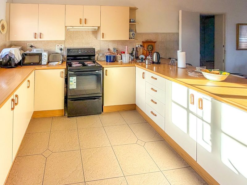A functional kitchen featuring laminate countertops, tiled flooring, a tiled backsplash, and built-in cabinetry with a freestanding stove and extractor fan.