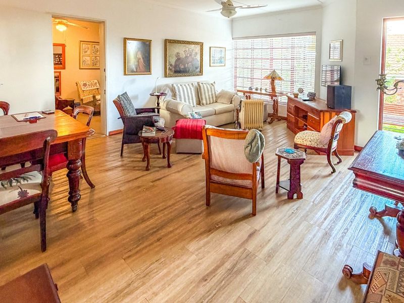 Spacious open-plan living and dining area featuring wood-look laminate flooring, a ceiling fan, and natural light through large windows and a sliding door.