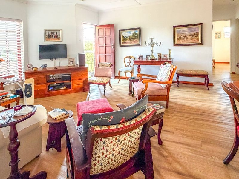 Spacious open-plan living and dining area featuring light-toned laminate flooring, large windows with venetian blinds, and direct access to an exterior entrance.
