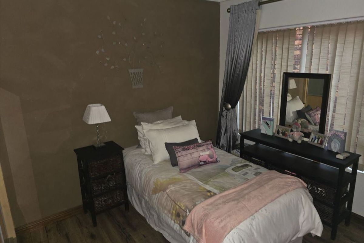 A cozy bedroom featuring laminate flooring, vertical blinds, and a neutral wall finish, providing a comfortable and functional sleeping space.