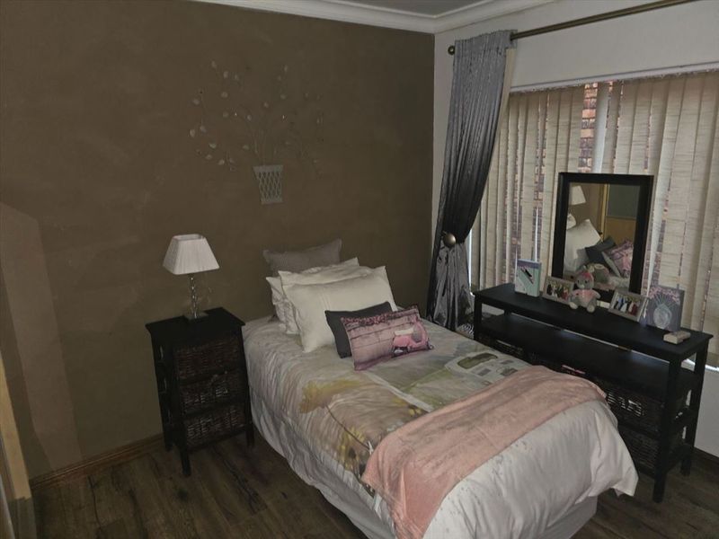 A cozy bedroom featuring laminate flooring, vertical blinds, and a neutral wall finish, providing a comfortable and functional sleeping space.