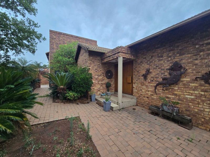 Front entrance of a face brick house featuring a paved walkway and a covered porch area with a wooden front door.