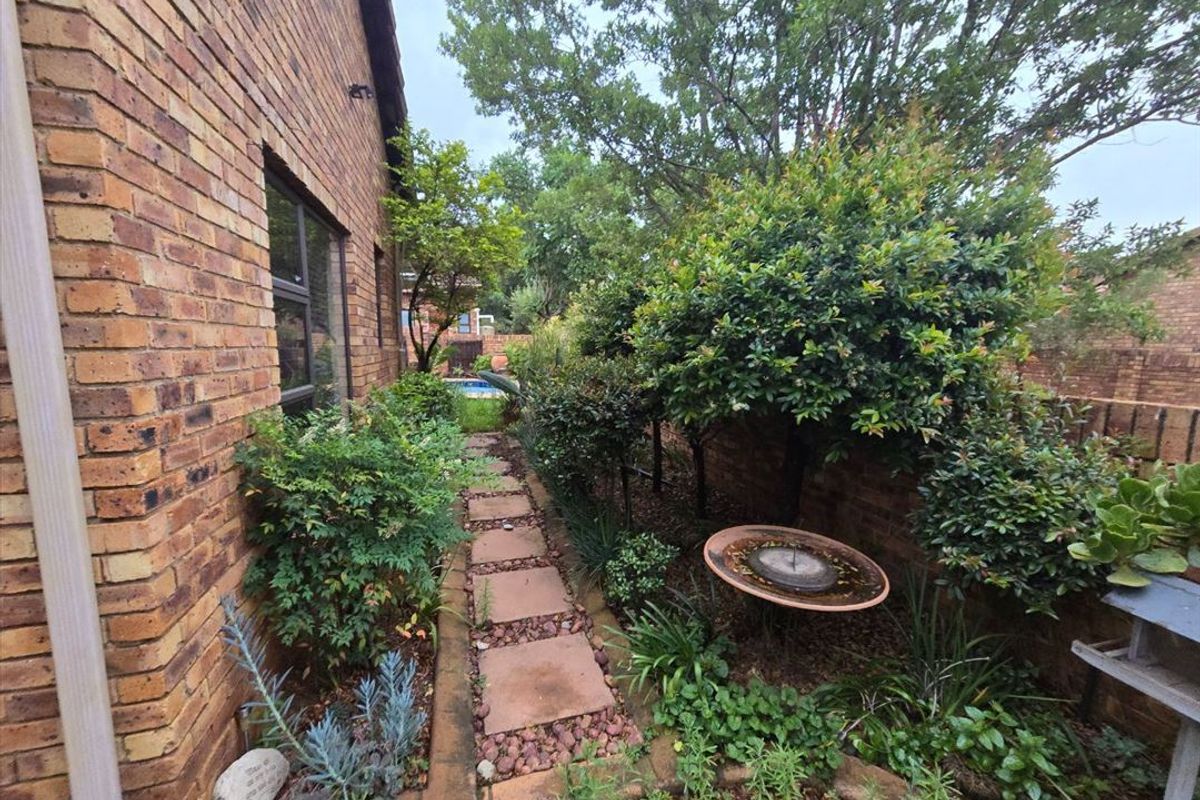 A side garden path featuring face brick exterior walls, established landscaping, and a paved walkway leading towards the rear of the property.