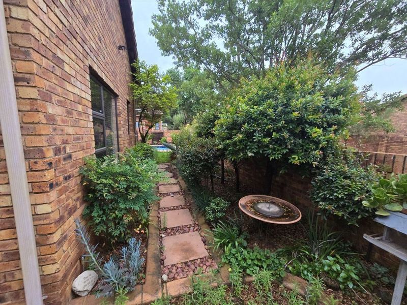 A side garden path featuring face brick exterior walls, established landscaping, and a paved walkway leading towards the rear of the property.