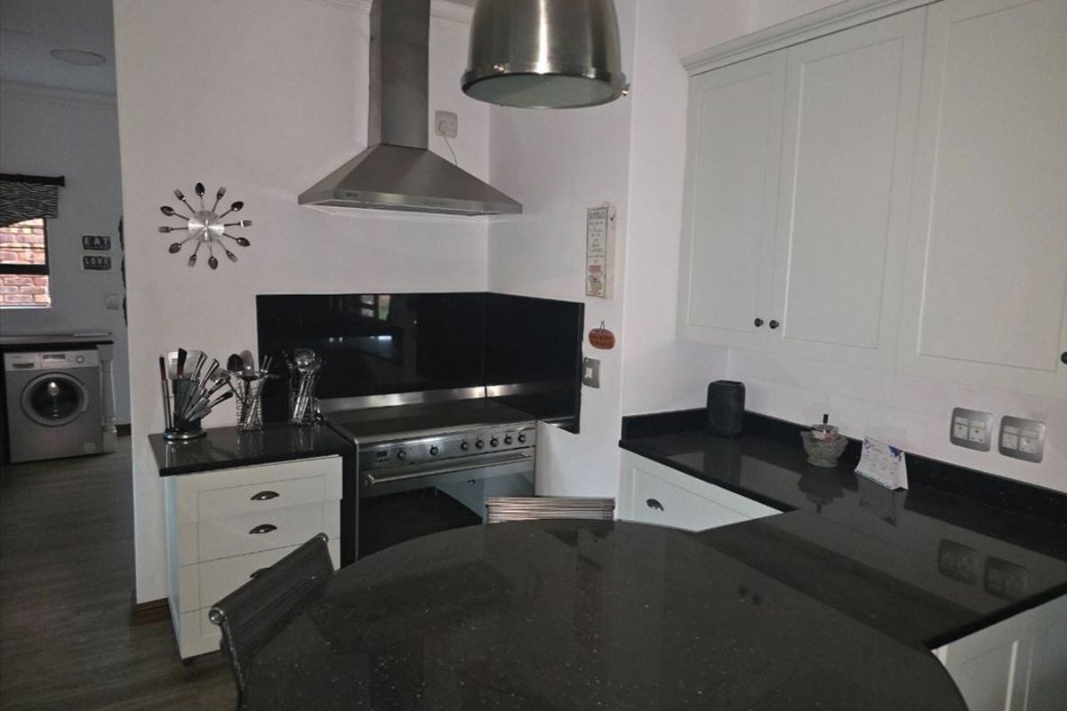 Modern kitchen featuring white cabinetry, dark granite countertops, stainless steel extractor fan, and a glass splashback, with an adjacent laundry area.