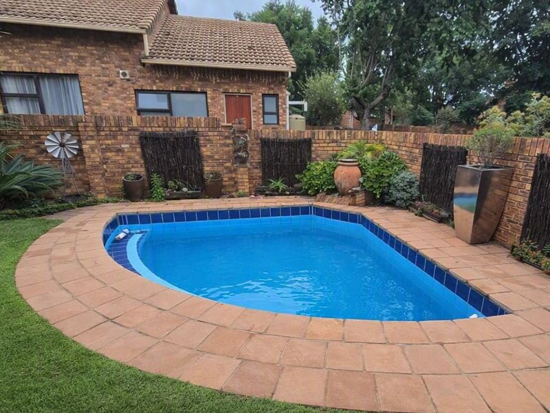 A private backyard featuring a swimming pool with a tiled surround, set against a brick boundary wall and landscaped garden area.