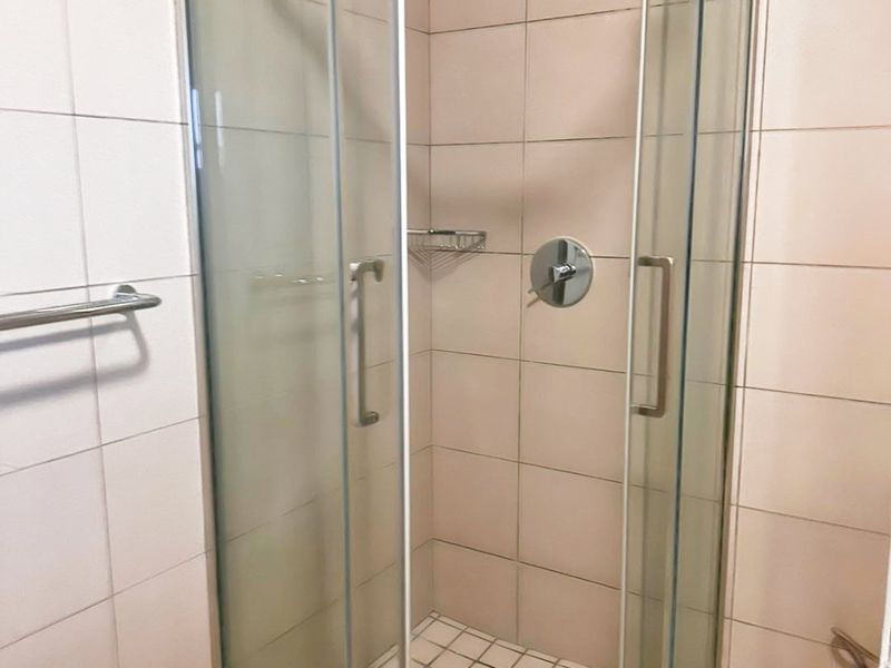A clean bathroom featuring a glass-enclosed shower with modern fixtures and neutral wall and floor tiling.