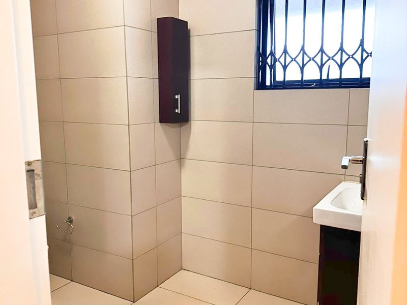 A clean, tiled bathroom featuring a vanity basin, wall-mounted storage cabinet, and a window secured with a metal security gate.