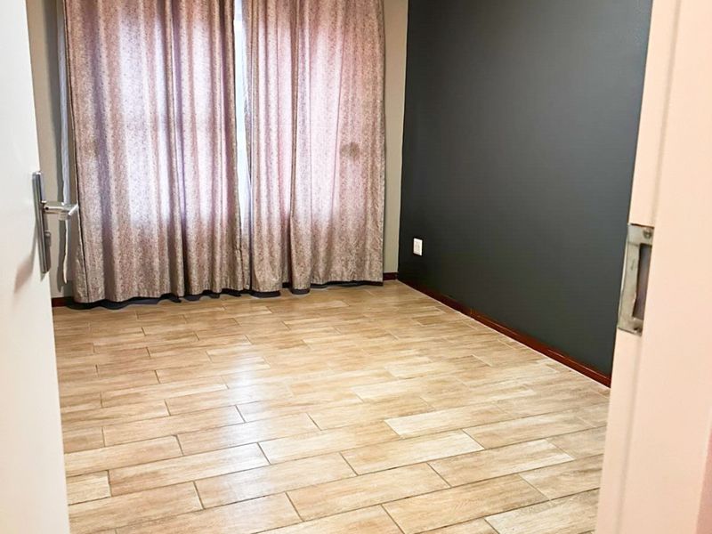 A bright, empty bedroom featuring wood-look tiled flooring and a dark accent wall, ready for personalization.