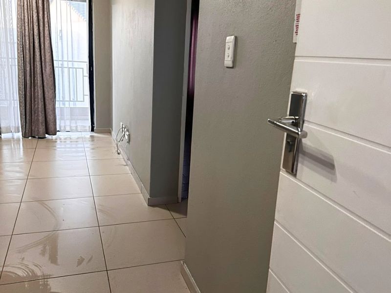 A vacant hallway featuring neutral tiled flooring and access to adjacent rooms, showing signs of wear on the floor surface.