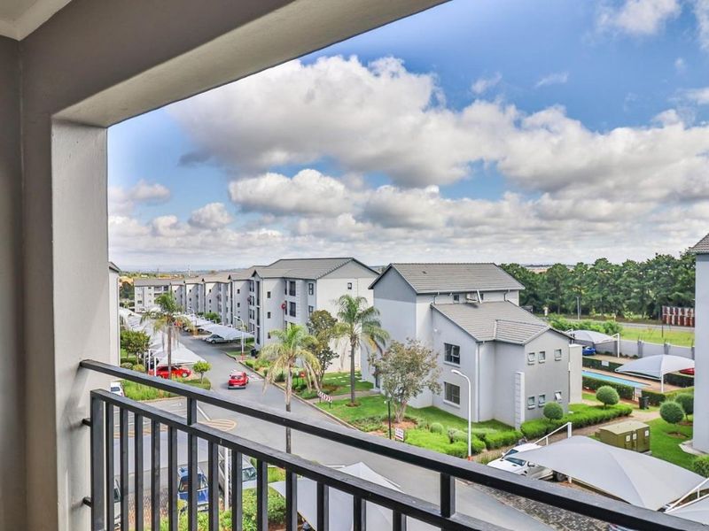 A view from a balcony overlooking the apartment complex grounds, parking areas, and surrounding landscape.