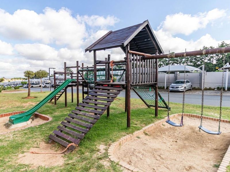 Outdoor communal playground area featuring a wooden jungle gym, slide, swing set, and sand pit with brick edging.