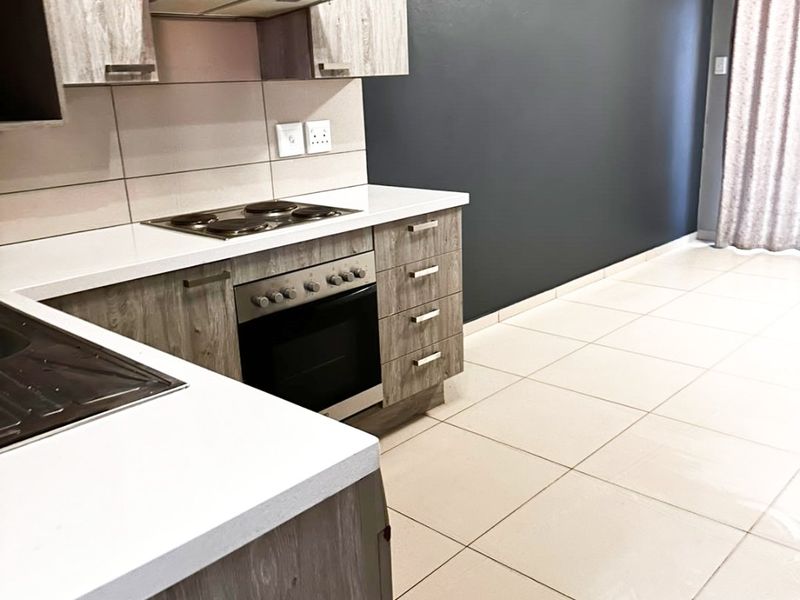 Modern kitchen featuring wood-grain cabinetry, built-in oven and hob, extractor fan, and neutral tiled flooring with a contrasting dark feature wall.