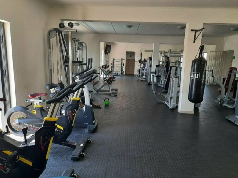 A functional apartment complex gym facility featuring durable rubber flooring, structural columns, and various fixed exercise equipment stations.