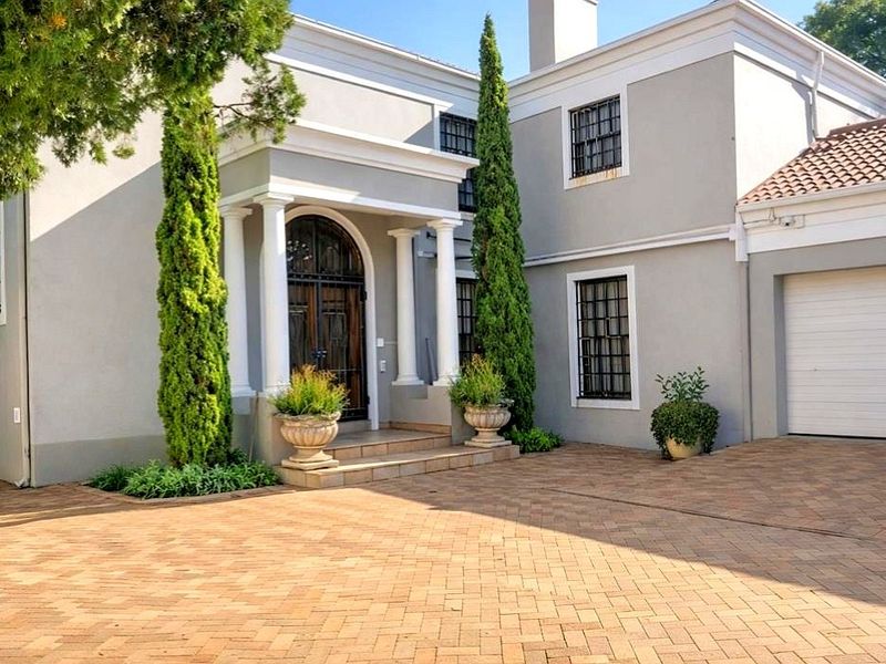 A well-maintained front facade featuring a paved driveway, double garage, and an elegant entrance with classical columns and an arched wooden door.