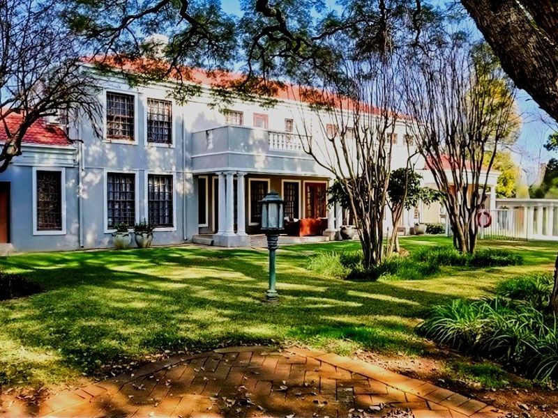 A spacious rear garden view of a two-story residence featuring a terracotta tiled roof, a balcony with columns, and a brick-paved patio area.