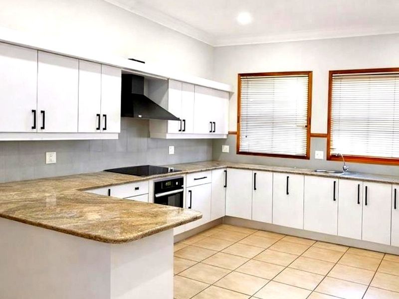 A clean, functional kitchen featuring white cabinetry, granite countertops, built-in appliances, and tiled flooring, offering a bright and practical workspace.