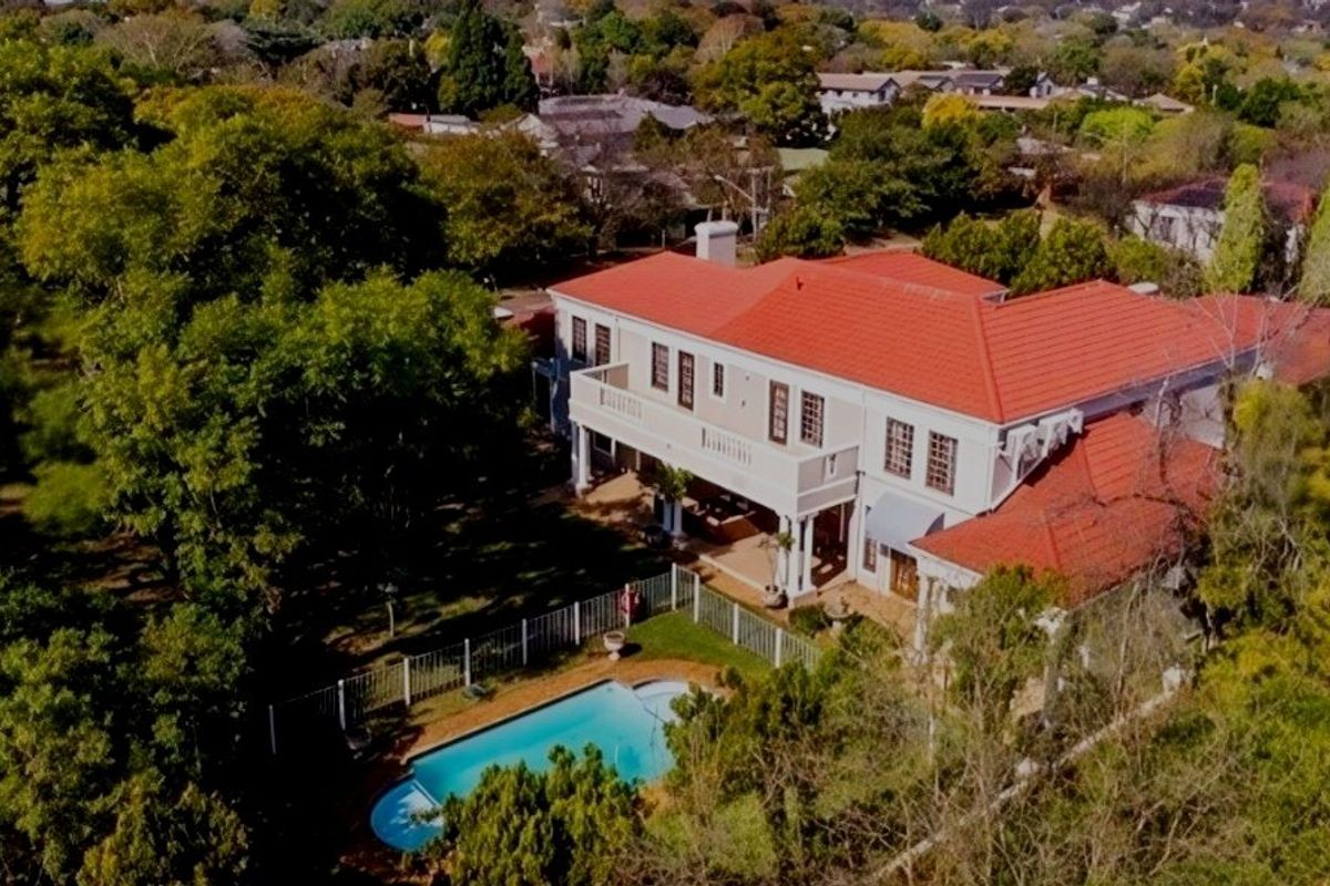 Aerial view of a large residential property featuring a tiled roof, upper-level balcony, and a private swimming pool set within a lush garden.