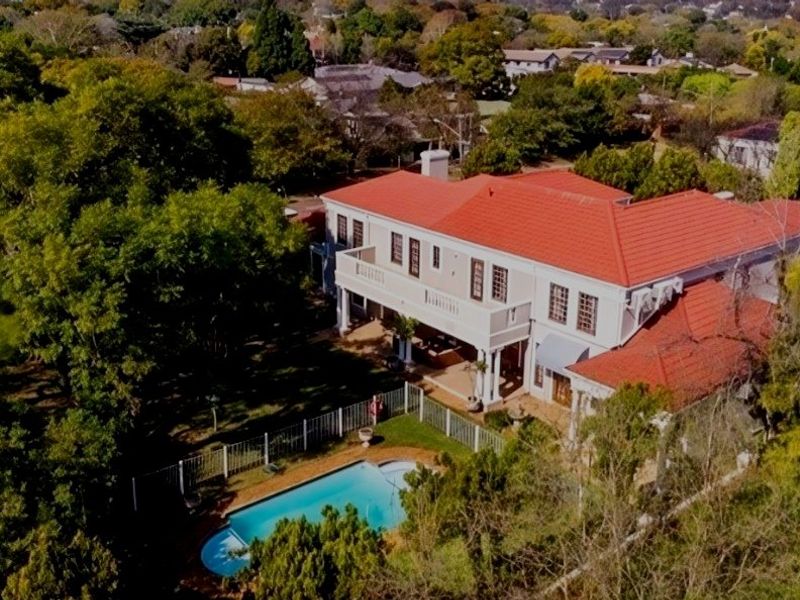 Aerial view of a large residential property featuring a tiled roof, upper-level balcony, and a private swimming pool set within a lush garden.