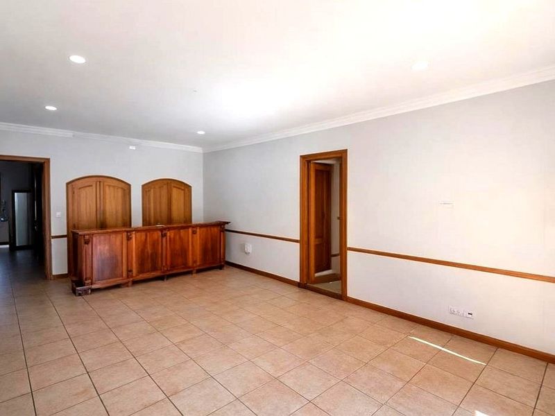 An empty room featuring a built-in wooden bar counter, tiled flooring, and recessed lighting, offering a versatile space for entertainment or living.