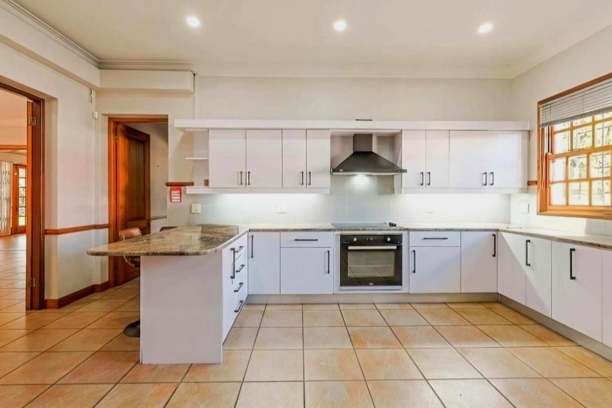 A clean, functional kitchen featuring white cabinetry, granite countertops, built-in oven and hob, and tiled flooring with recessed lighting.