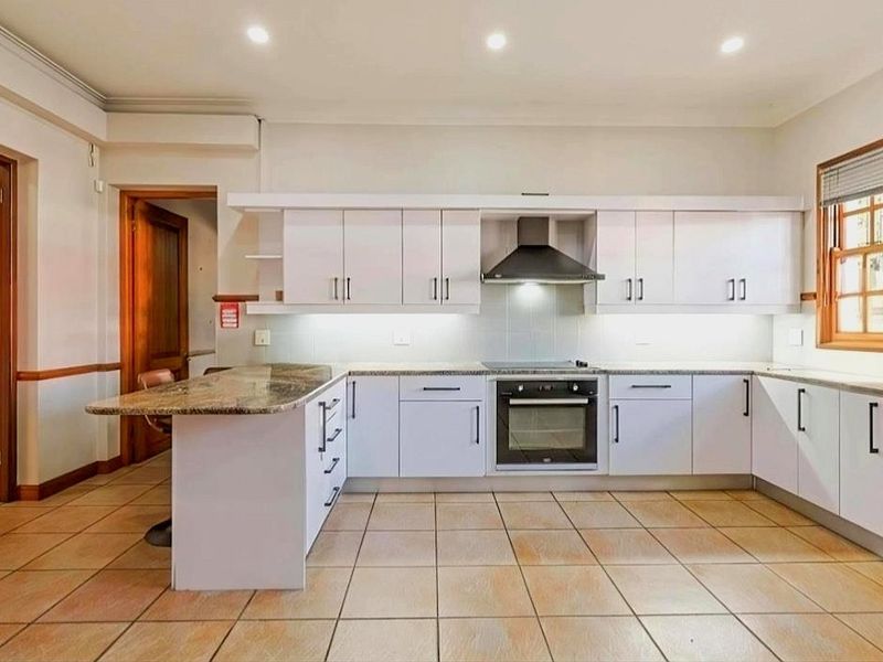 A clean, functional kitchen featuring white cabinetry, granite countertops, built-in oven and hob, and tiled flooring with recessed lighting.