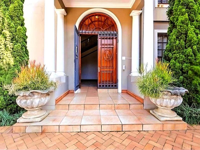 A grand front entrance featuring an arched wooden door with security gate, flanked by classical columns and set above tiled steps.