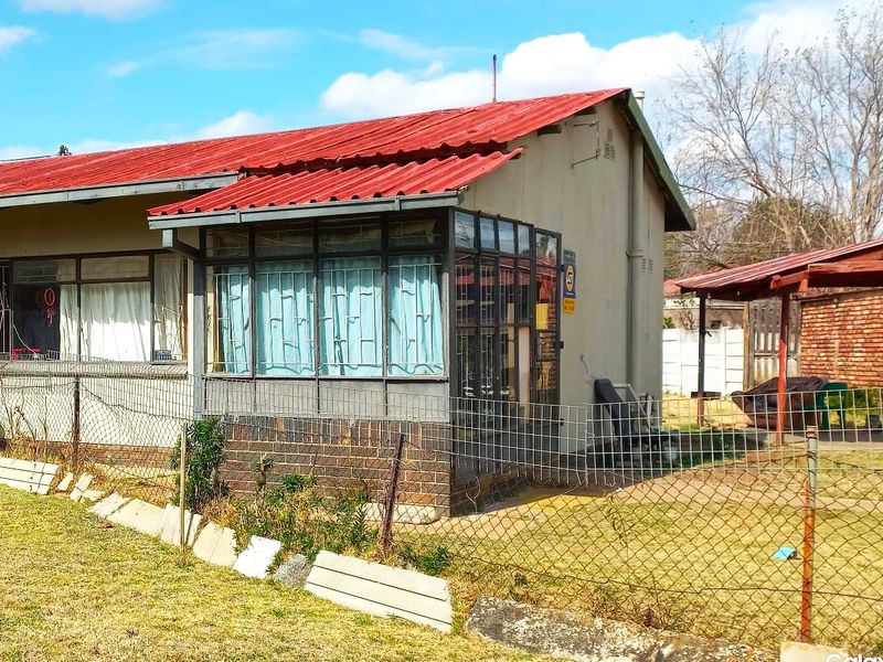 Rear view of the property featuring a corrugated metal roof, an enclosed patio area, and a fenced garden space with a covered outdoor structure.