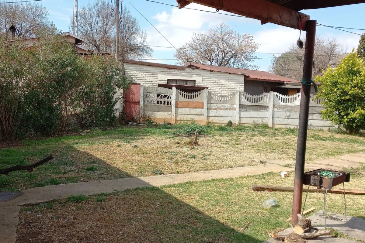 A rear garden area featuring a lawn, concrete pathways, and a precast concrete boundary wall.