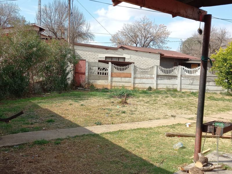 A rear garden area featuring a lawn, concrete pathways, and a precast concrete boundary wall.