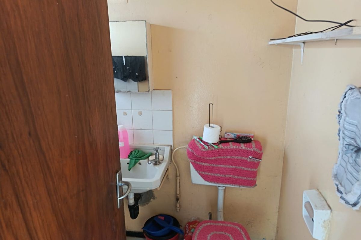 A compact bathroom featuring a wall-mounted basin, toilet cistern, and tiled splashback, currently requiring cosmetic updates and maintenance to the wall finishes.