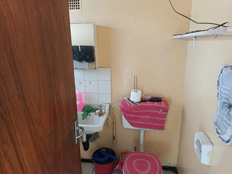 A compact bathroom featuring a wall-mounted basin, toilet cistern, and tiled splashback, currently requiring cosmetic updates and maintenance to the wall finishes.