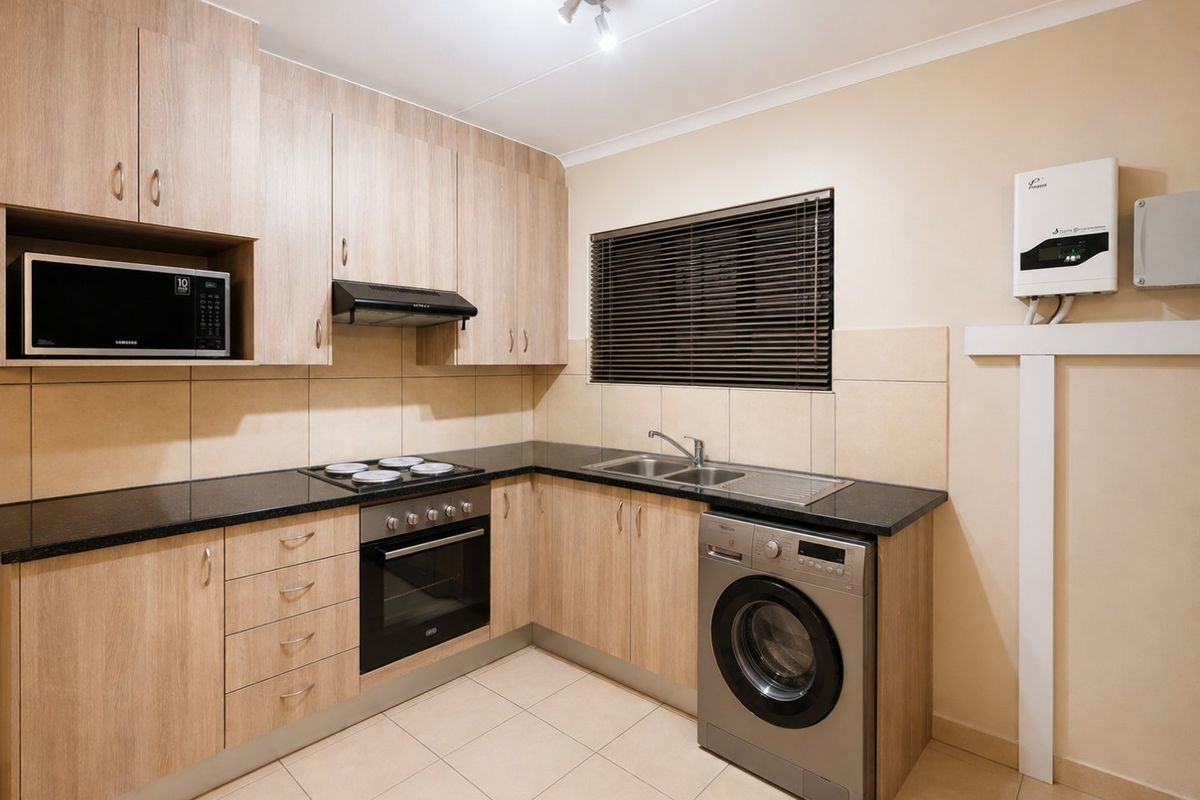 Modern kitchen featuring light wood-finish cabinetry, granite countertops, built-in oven, electric hob, and integrated laundry plumbing, finished with neutral floor and wall tiling.