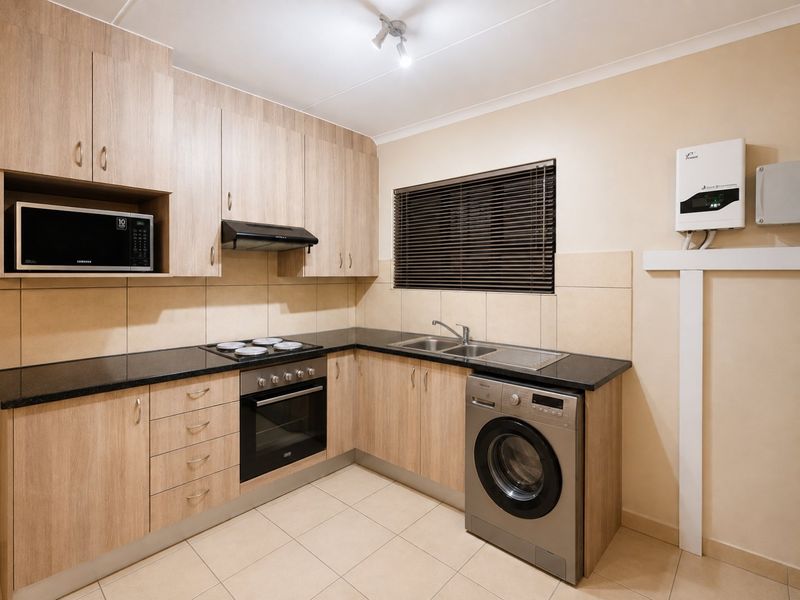 Modern kitchen featuring light wood-finish cabinetry, granite countertops, built-in oven, electric hob, and integrated laundry plumbing, finished with neutral floor and wall tiling.