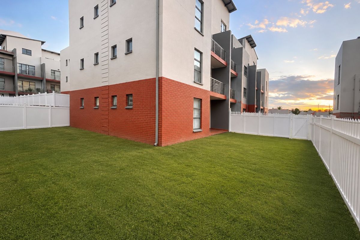 A view of the rear exterior of the apartment building featuring a well-maintained lawn and white vinyl perimeter fencing.