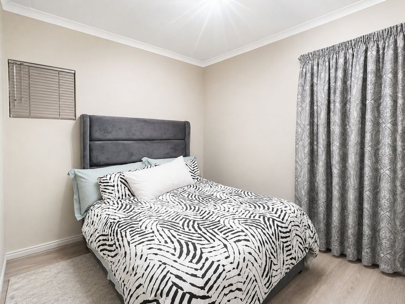 A well-maintained bedroom featuring neutral wall tones, laminate flooring, a venetian blind, and full-length curtains.