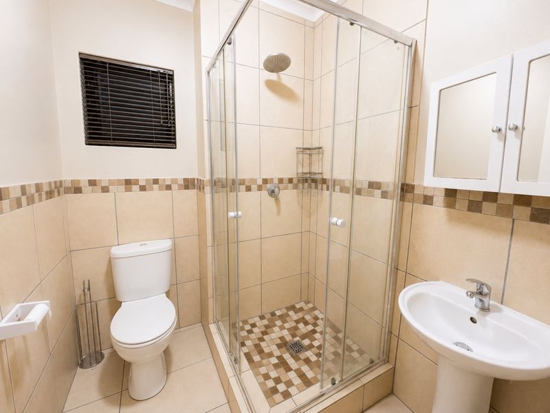 A clean, functional bathroom featuring a glass shower enclosure, pedestal basin, toilet, and neutral tiled finishes throughout.