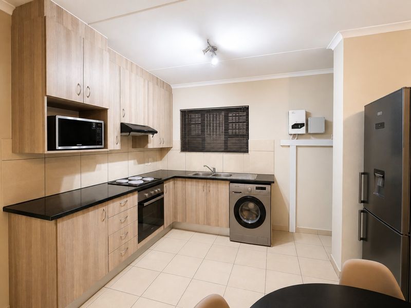 Modern kitchen featuring light wood cabinetry, black countertops, integrated appliances, and tiled flooring, offering a clean and functional workspace.