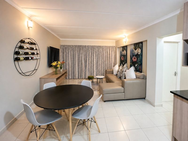 A well-maintained open-plan living and dining area featuring neutral tiled flooring, modern cove cornicing, and wall-mounted lighting fixtures.