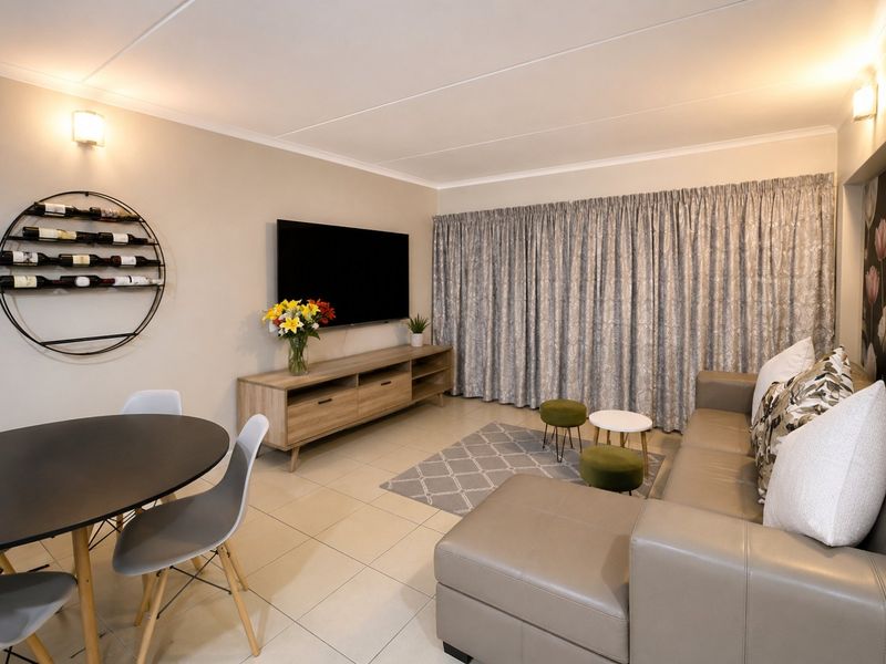 A well-maintained open-plan living and dining area featuring neutral tiled flooring, coved ceilings, and wall-mounted lighting fixtures.
