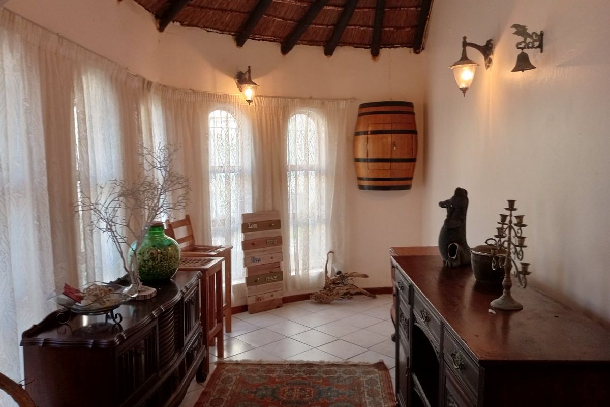 A cozy living area featuring a traditional thatched ceiling with exposed timber rafters, tiled flooring, and arched windows that provide natural light.
