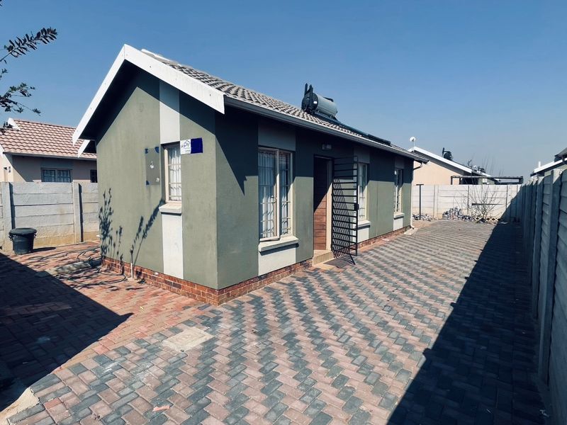Rear view of a detached house featuring a paved yard, precast boundary walls, and a roof-mounted solar geyser system.