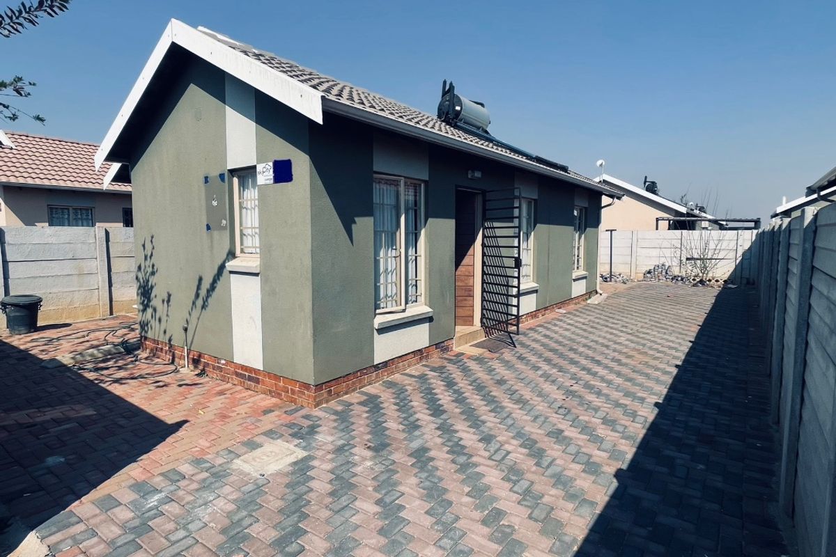 Rear view of a detached house featuring a paved yard, solar geyser, and secure boundary walling.