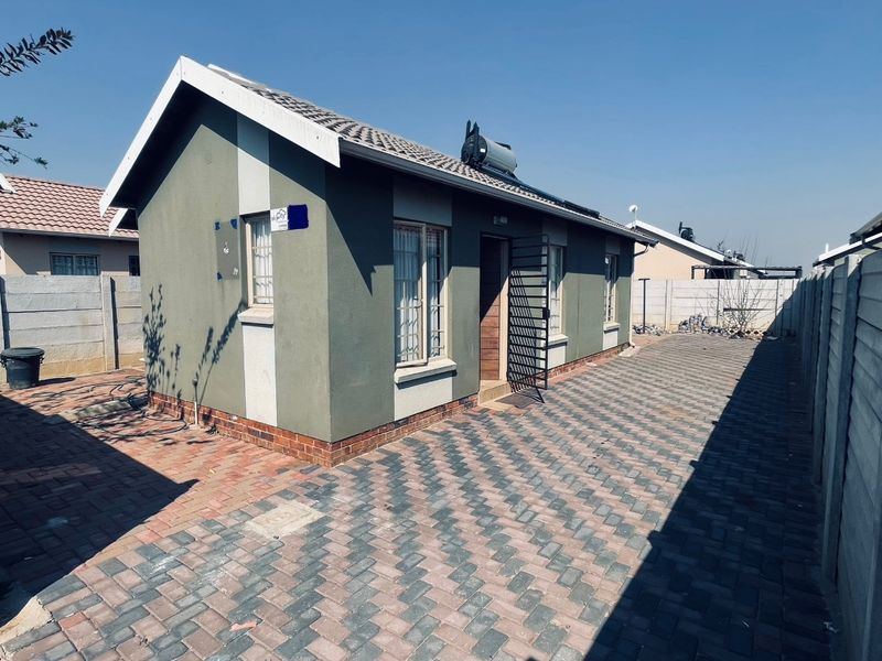 Rear view of a detached house featuring a paved yard, solar geyser, and secure boundary walling.